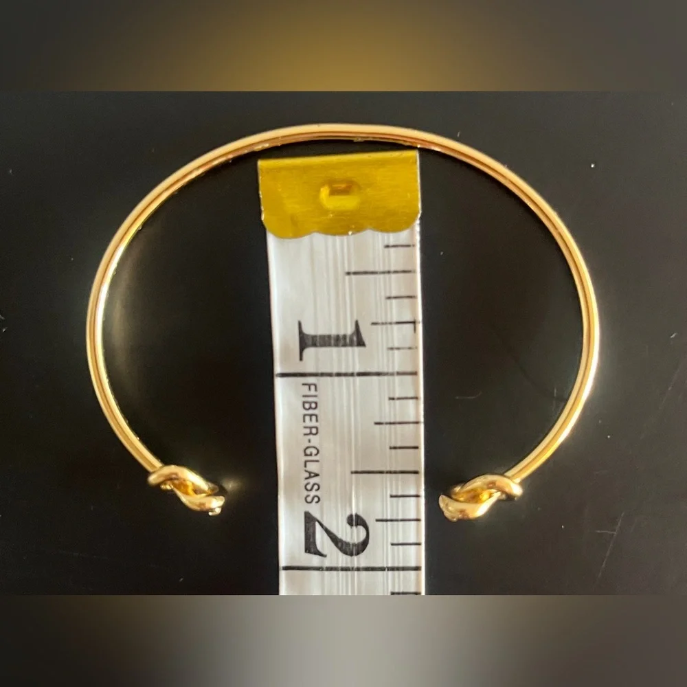 Kate Spade New York Loves Me Knot Cuff bangle in gold-tone w knot-accented ends.
